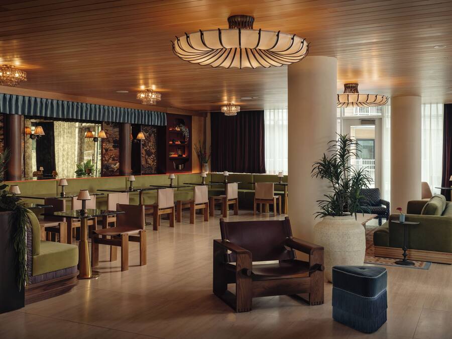 A spacious lobby with a high ceiling, wooden flooring, and a variety of seating options including sofas, chairs, and a bar area.
