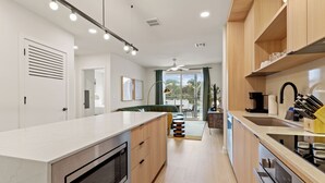Une cuisine moderne dotée d’un îlot central, d’appareils électroménagers intégrés et offrant une vue sur l’extérieur.