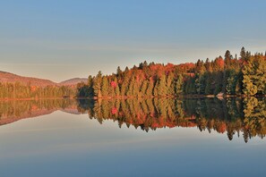A calm lake reflecting a forest with autumn foliage.