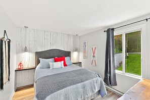 A bedroom with a bed, bedside tables, a window with curtains, and a view of greenery outside.