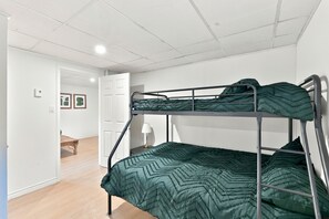A bunk bed with a green patterned bedspread in a room with white walls and a wooden floor. - 5 minutes from Mont-Garceau! Water House with Spa in Saint-Donat. (Saint-Donat)