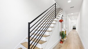 Moderni portaikko, jossa on puiset askelmat ja mustat kaiteet, johtaa aulaan, jossa on punainen lattiavalaisin ja ruukussa oleva kasvi.