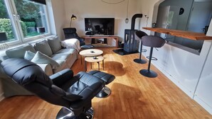 Ein modernes Wohnzimmer mit einer Couch, einem schwarzen Sessel, einem Fernseher, einem Kaminofen und einer Bar.