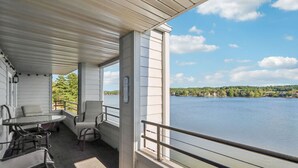 A covered balcony with a table and chairs, overlooking a calm lake and forested shoreline. - Jana`s Penthouse, Fireplace, Skiing, Boating (Wisconsin Dells)