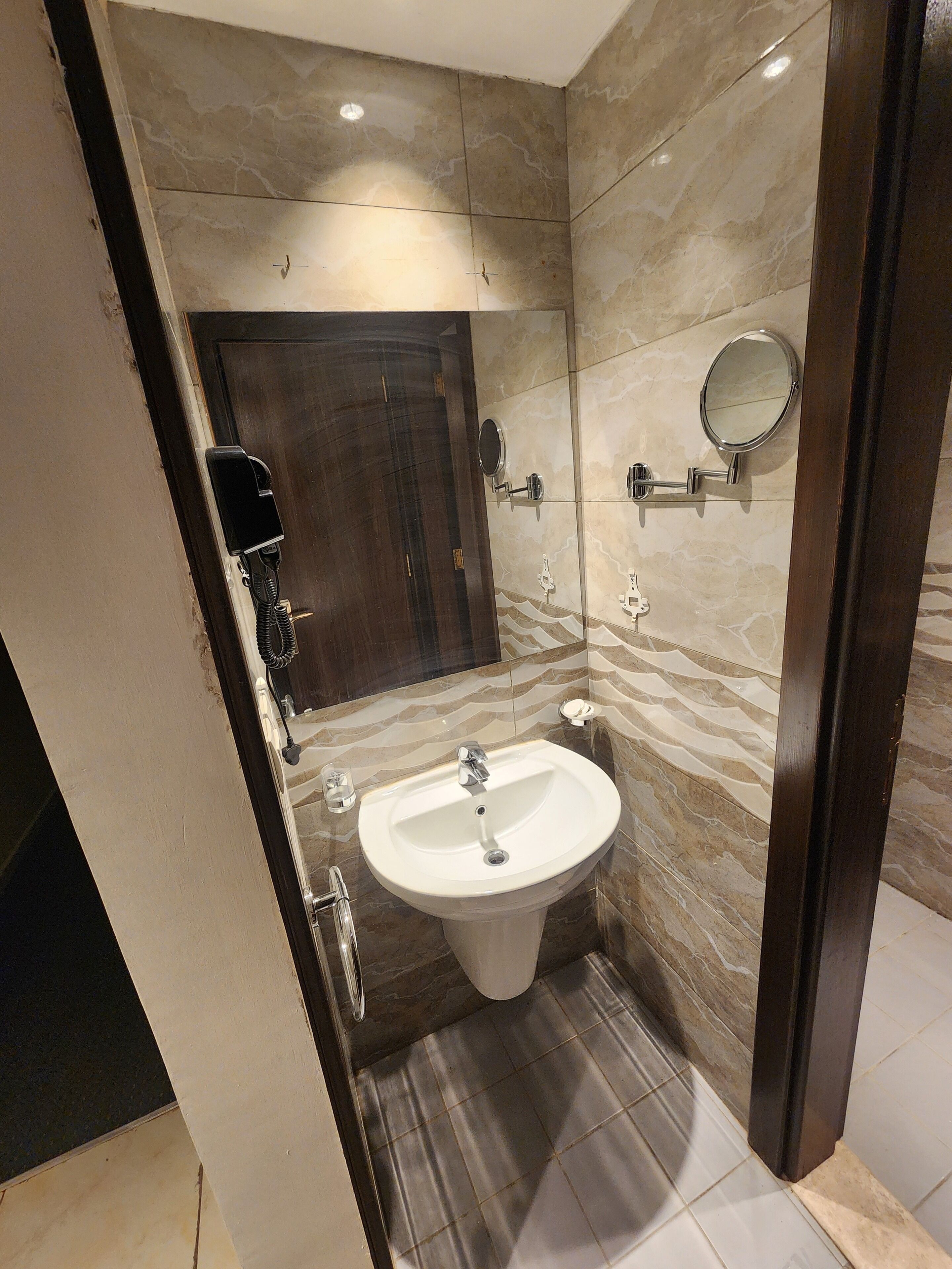 A bathroom with a marble wall, a sink, a mirror, and a hairdryer.