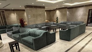 A spacious lobby with a modern design, featuring a large seating area with sofas and a coffee table, a marble floor, and recessed lighting.