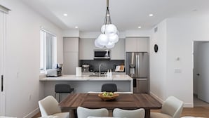 Een moderne keuken met een centraal eiland, roestvrijstalen apparatuur en een eethoek met een houten tafel en stoelen.
