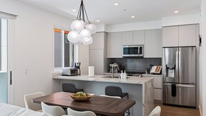Een moderne keuken met een centraal eiland, roestvrijstalen apparatuur en een eethoek met een houten tafel en stoelen.