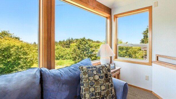 A room with a large window, a blue sofa, a patterned pillow, and a lamp on a wooden nightstand. - Pet-friendly Oceanfront Getaway (Rockaway Beach)