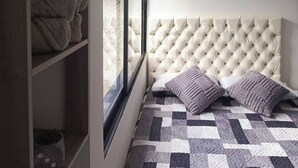 Ein Schlafzimmer mit einer gepolsterten Kopfteile, einer gesteppten Bettdecke und einem Fenster mit Blick ins Freie.
