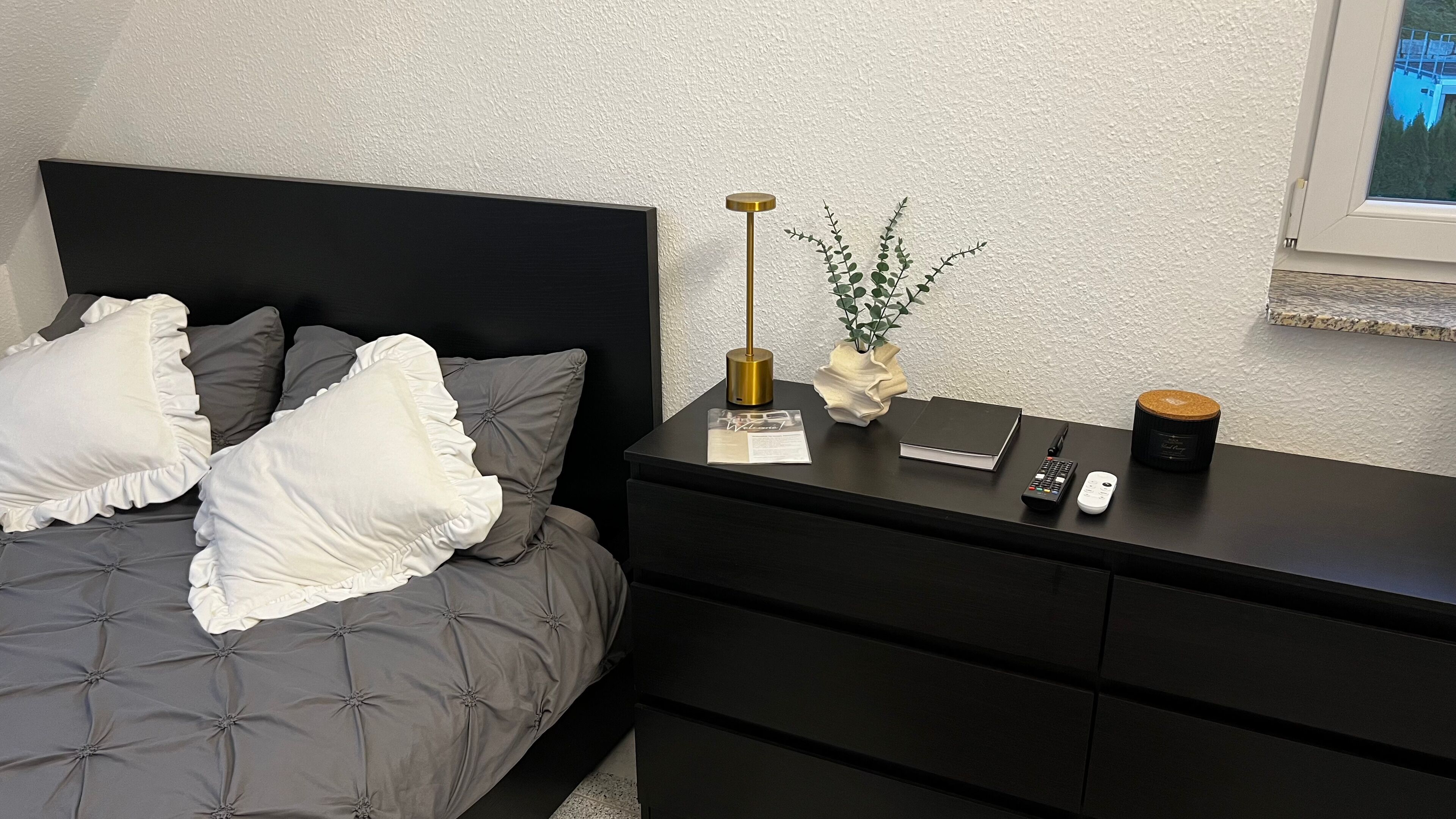 A neatly arranged bedroom with a bed, bedside table, and a window.