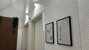 Un pasillo con un cartel enmarcado que enumera las normas de la casa, un cartel enmarcado con la palabra 'Wifi' y una puerta con una planta en la pared.