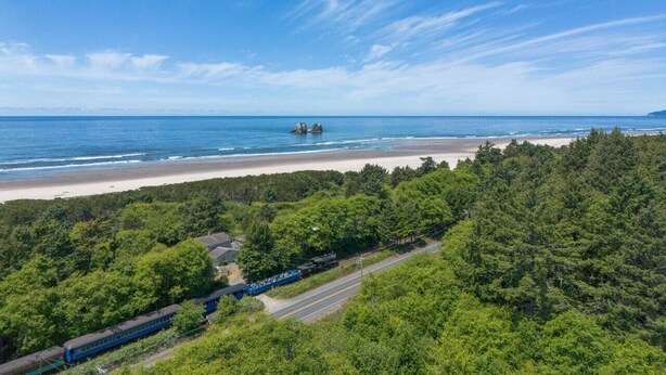 Een kustlandschap met een strand, dicht bos en een treinspoor.