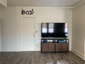 A room with a television on a wooden cabinet, a door with a 'local' sign, and a patterned rug.