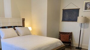 Ein Schlafzimmer mit einem Bett, einer Bank, einer Lampe und einem gerahmten Bild an der Wand.