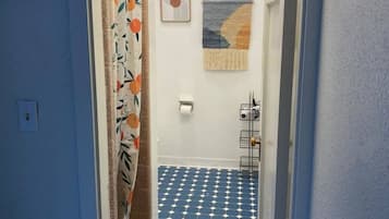 A narrow hallway with a patterned floor, a door with a floral curtain, and a wall-mounted towel rack.