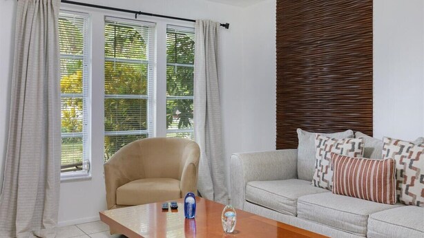 A living room with a beige sofa, a wooden coffee table, and a window with blinds. - Costerra Naples 2BED (Naples)