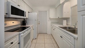A compact kitchen with white cabinetry, a microwave, an oven, a refrigerator, and a sink. - Costerra Naples 2BED (Naples)