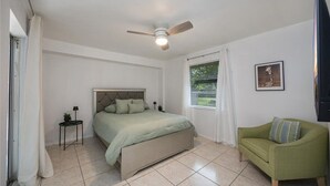 A bedroom with a bed, a green sofa, a ceiling fan, a window with curtains, and a framed picture on the wall. - Costerra Naples 2BED (Naples)