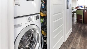 Un cuarto de lavandería con dos lavadoras de carga frontal apiladas y un estante empotrado con útiles de lavandería.