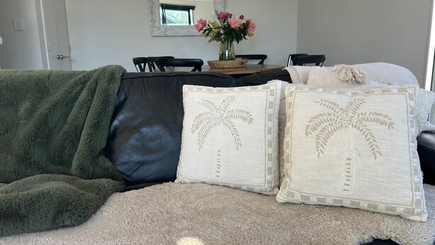 A cozy living room with a green furry couch, a black leather sofa, and two decorative pillows with palm tree designs. - 
The Park 
Modern,sun-filled two-bedroom townhouse, with free off-street parking (Christchurch)