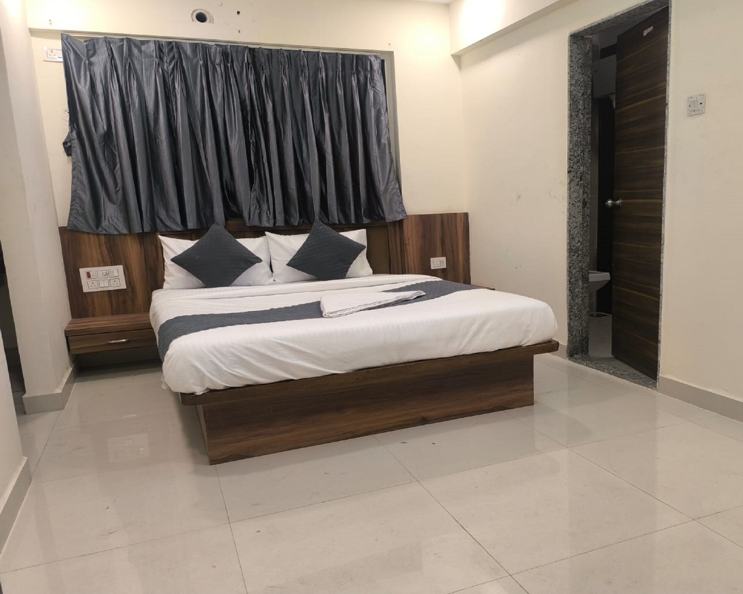 A modern bedroom with a wooden bed frame, white bedding, and a dark curtain.