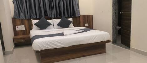 A modern bedroom with a wooden bed frame, white bedding, and a dark curtain.