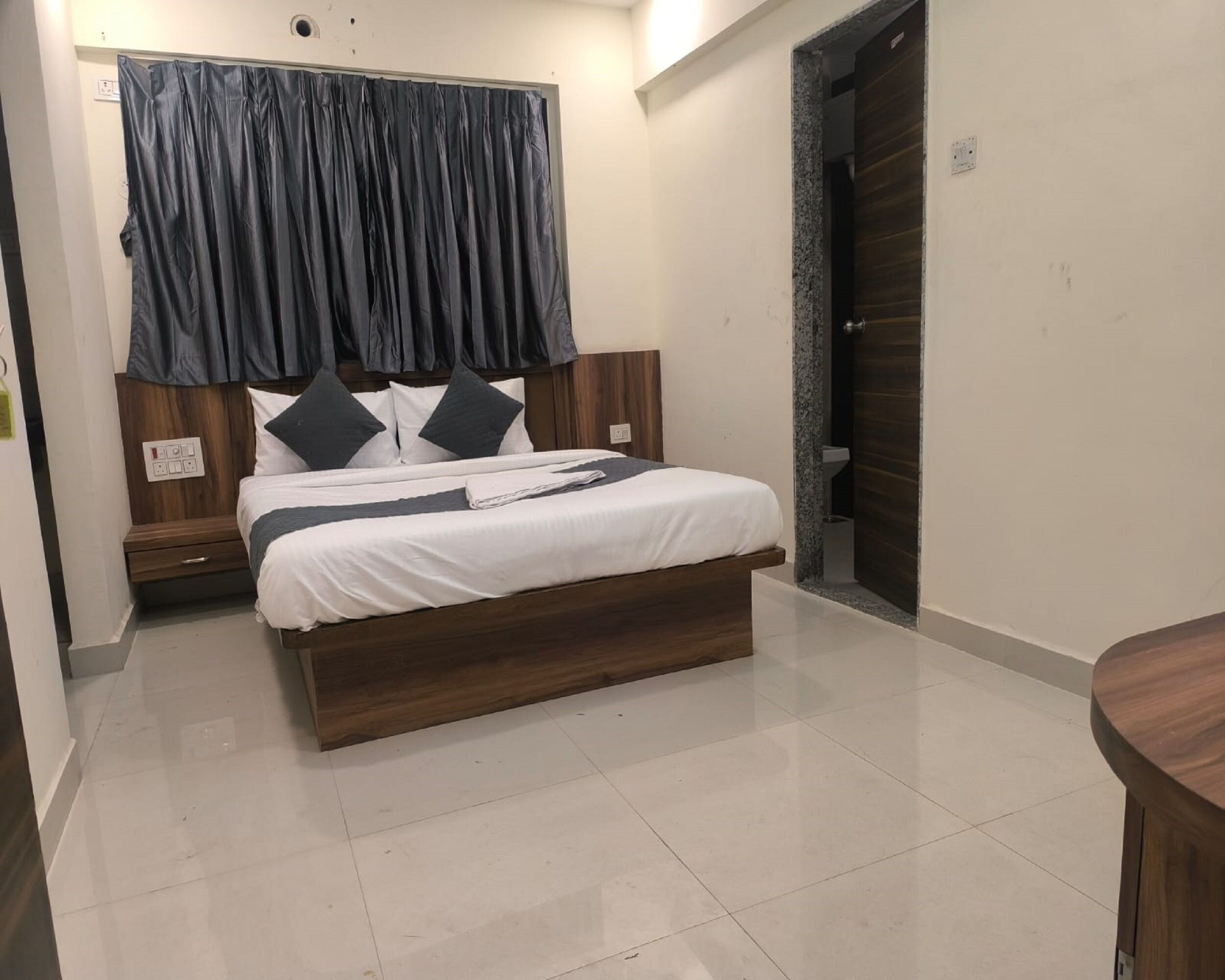 Un dormitorio moderno con una cama de madera, ropa de cama blanca y una cortina oscura.