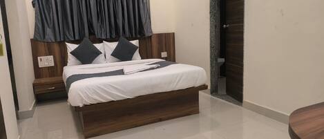 Un dormitorio moderno con una cama de madera, ropa de cama blanca y una cortina oscura.