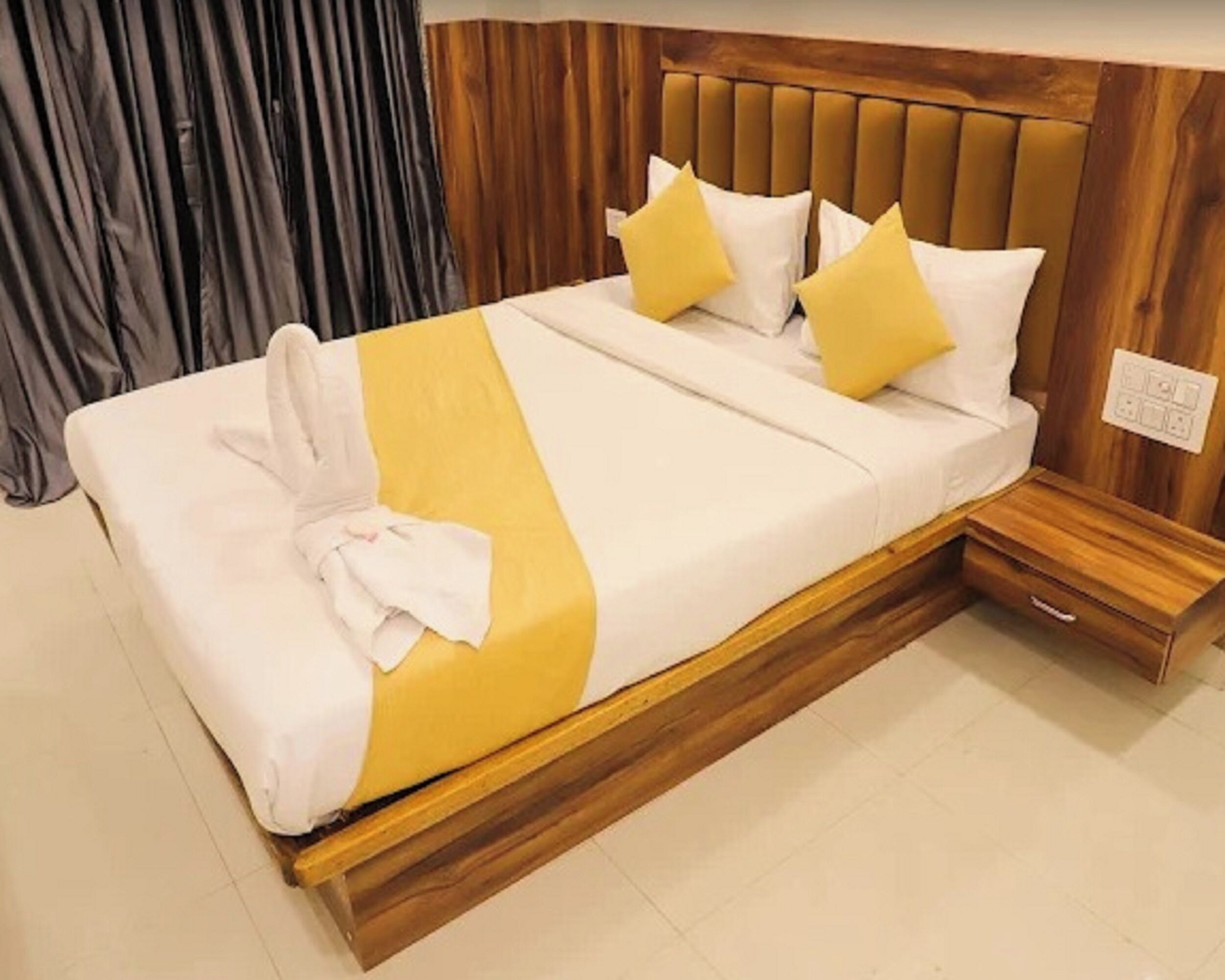 A neatly made bed with a yellow and white bedspread, two pillows, and a white towel on the side.