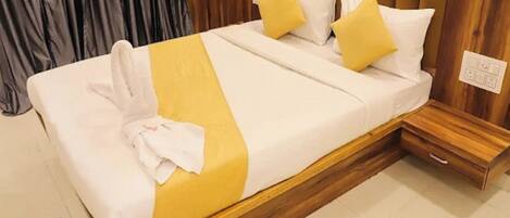 A neatly made bed with a yellow and white bedspread, two pillows, and a white towel on the side.