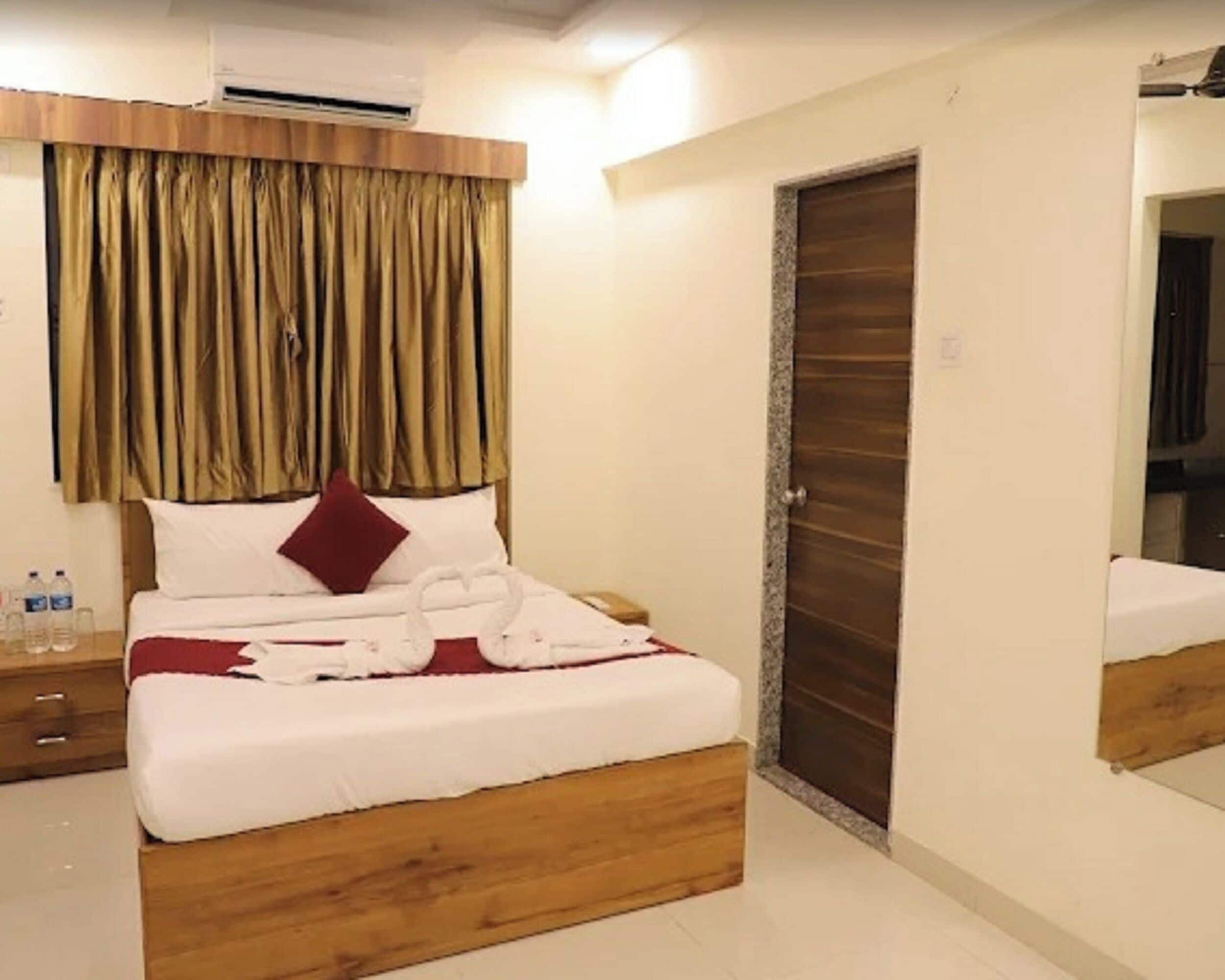 A hotel room with a wooden bed frame, white bedding, a red pillow, and a large mirror on the wall.