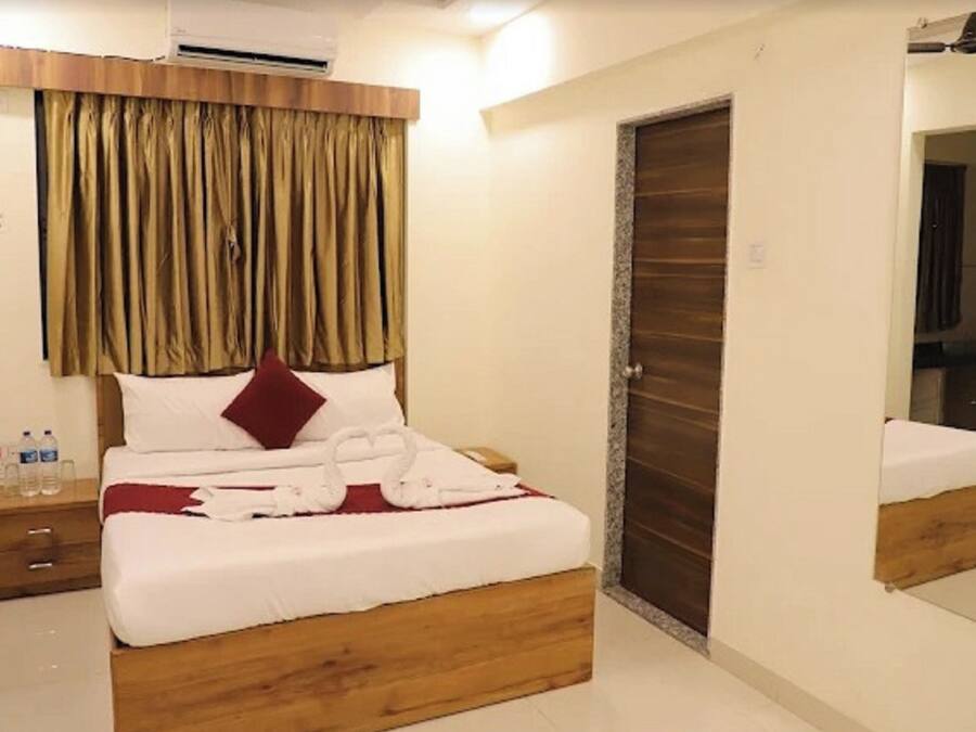 A hotel room with a wooden bed frame, white bedding, a red pillow, and a large mirror on the wall.