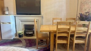 Ein Zimmer mit Esstisch, Stühlen, Fernseher, Kühlschrank und Kamin.