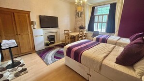 Ein Schlafzimmer mit zwei Betten, einem Fernseher, einem Kamin, einem Esstisch mit Stühlen und einer Chandelier.