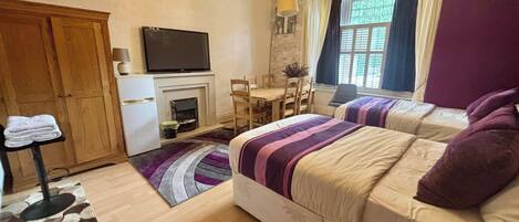 A bedroom with two beds, a television, a fireplace, a dining table with chairs, and a chandelier.