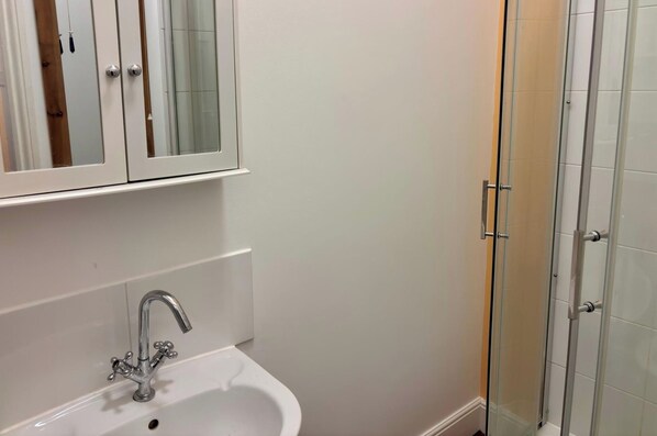 A bathroom with a white sink, a mirror above it, and a glass shower enclosure. - Sandon Apartment Oasis in Birmingham (Birmingham)