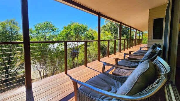Une terrasse extérieure couverte, dotée de chaises en osier et d’une table en bois, qui offre une vue sur une zone boisée.