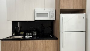 A compact kitchen with a microwave, refrigerator, and black countertop. - Sabana Urbana (San José)