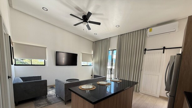 A modern kitchen with a central island, a ceiling fan, and a flat-screen TV mounted on the wall. - Sabana Urbana (San José)