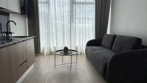 A modern living room with a dark grey sofa, a small round coffee table, and a kitchen area with a dark countertop and cabinets. - Sabana Urbana (San José)
