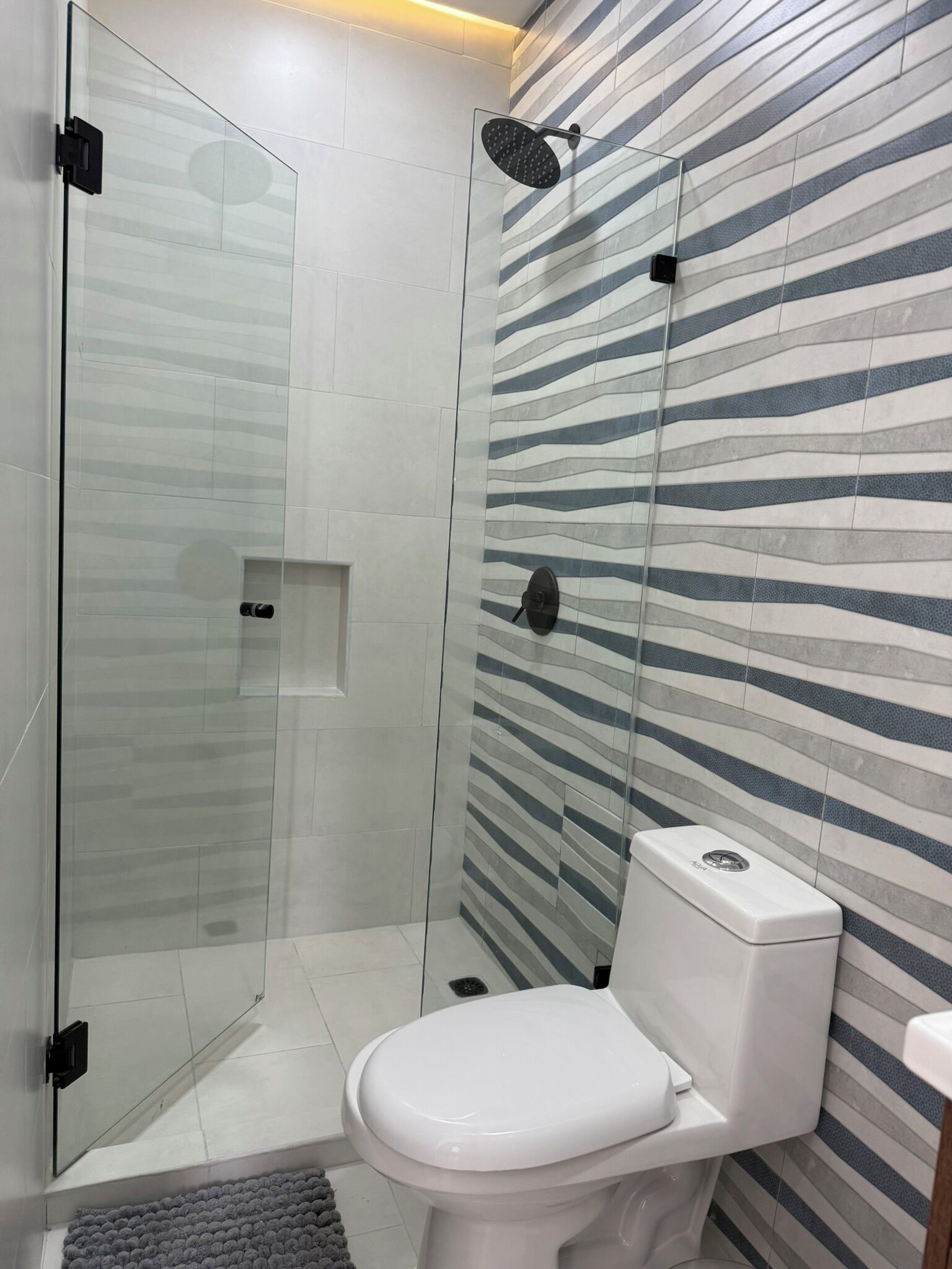 A modern bathroom with a glass shower enclosure, a white toilet, and a striped tile wall.