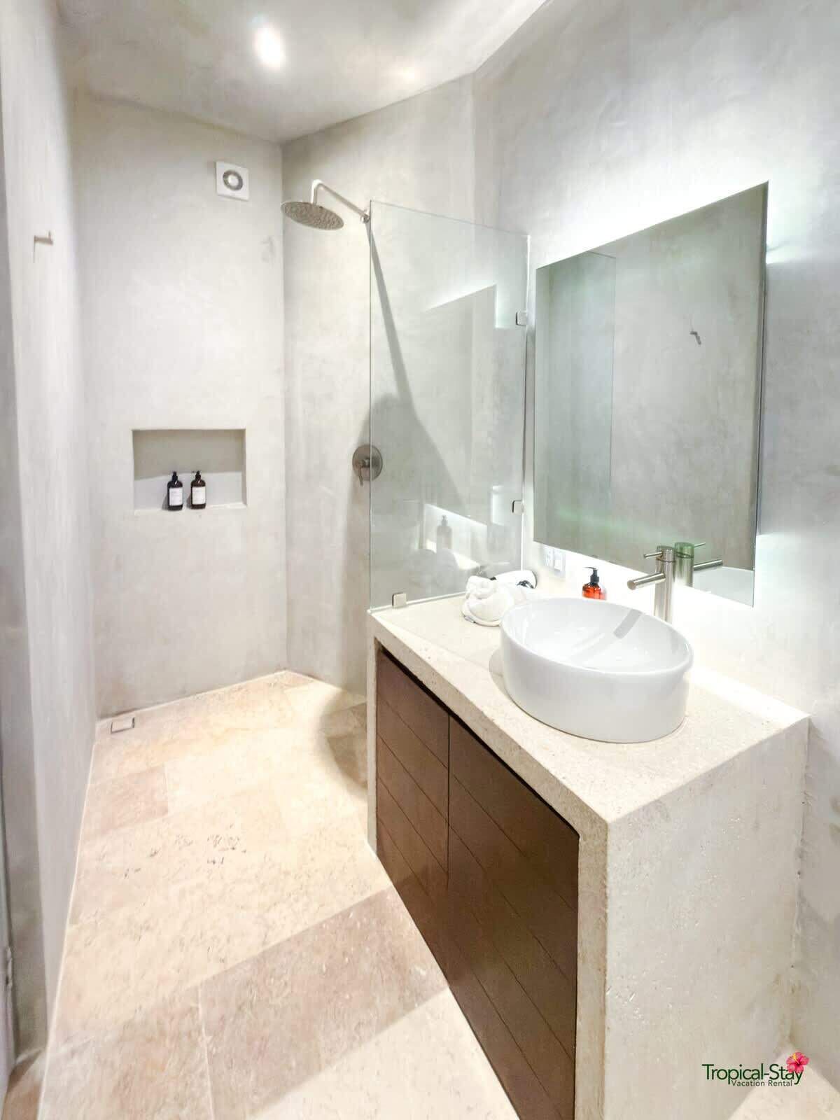 Une salle de bain moderne avec un grand miroir, un lavabo rond et une douche.