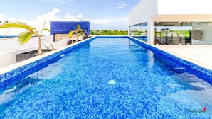 Une piscine avec un bord carrelé, un palmier et un bâtiment moderne doté d’une façade en verre.