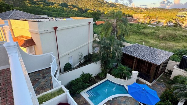 A rooftop pool area with a blue umbrella, a small wooden structure, and a view of a hilly landscape in the background. - Breathtaking villa with private pool and hot tub, 2 minute walk from the beach. (Gros Islet)