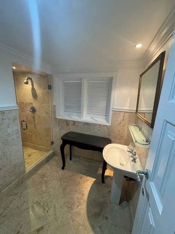 A bathroom with a walk-in shower, a vanity with a mirror, and a bench.