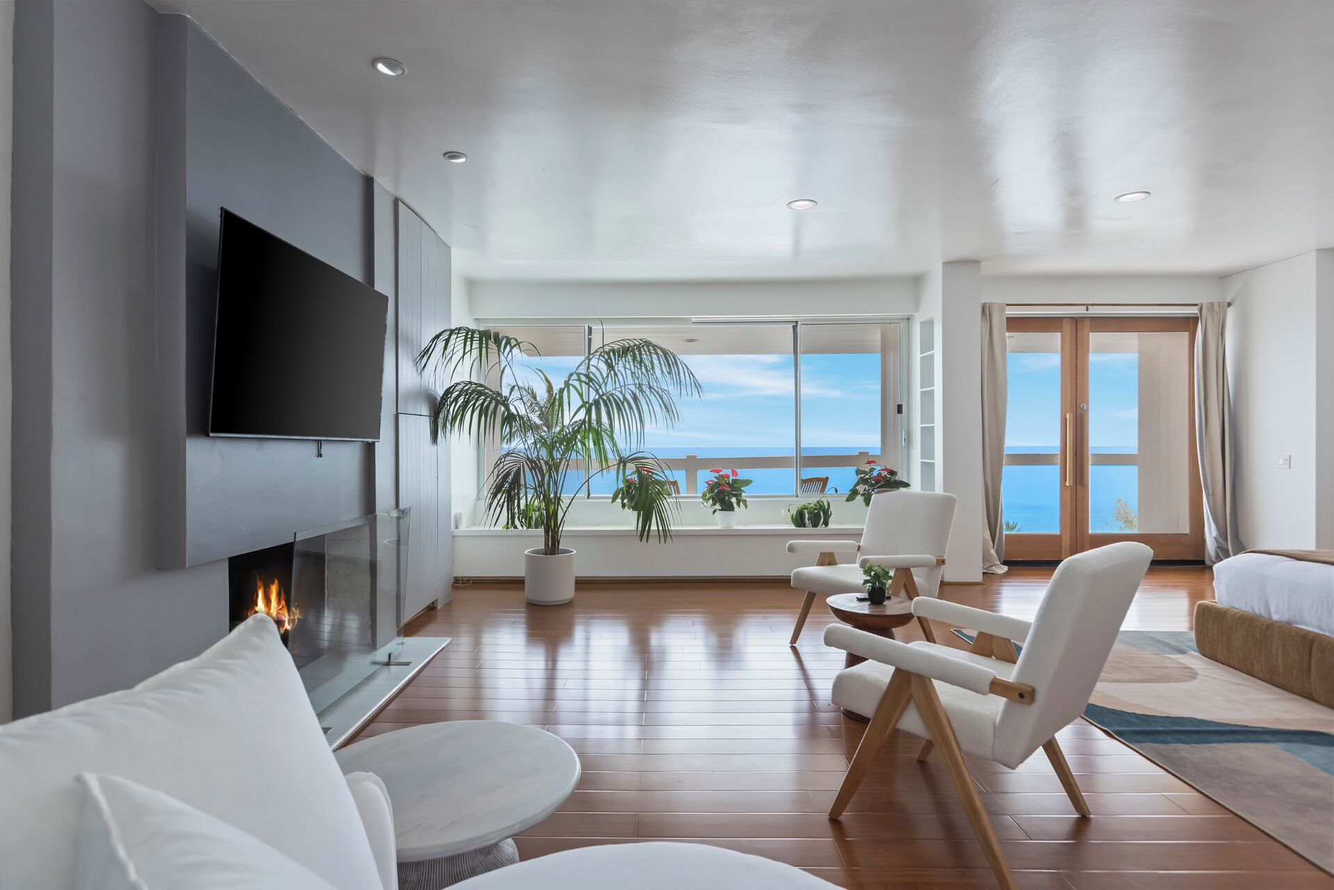 A modern living room with a flat-screen TV, a fireplace, and a large window with a view of the sea.