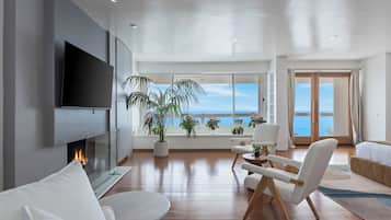 A modern living room with a flat-screen TV, a fireplace, and a large window with a view of the sea.