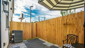 A patio area with a wooden fence, a black outdoor heater, a metal table with a chair, and a striped umbrella.
