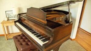 Um piano de cauda com um banquinho, uma lâmpada e um quadro emoldurado sobre uma mesinha ao lado.